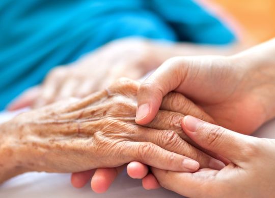 Woman holding senior woman's hand on bed